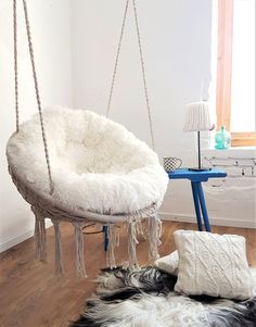 a white hanging chair on a wooden floor next to a blue table and black sheepskin rug