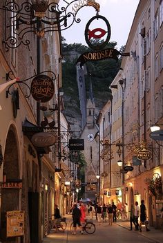 an alley way with people walking and shopping on the sidewalks in front of buildings at dusk