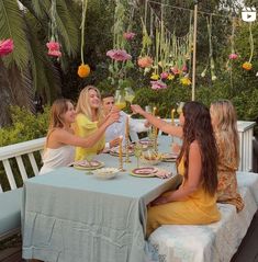 four women sitting at a table toasting with wine glasses in front of them and flowers hanging from the ceiling