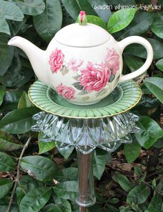 a tea pot sitting on top of a glass stand in front of some green leaves