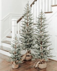 two small christmas trees sitting on top of a wooden floor next to a banister