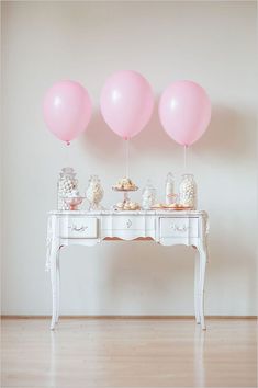 three pink balloons sitting on top of a table next to a white dresser with candy