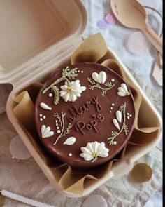 there is a chocolate cake with flowers on it in a box next to spoons