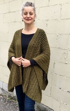 a woman standing in front of a brick wall wearing a green knitted cardigan