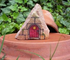 a rock shaped like a house with a red door in the center and green plants behind it