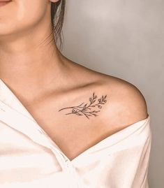 a woman wearing a white shirt has a tattoo on her shoulder and is looking off to the side