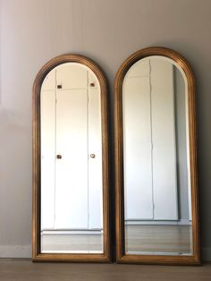 two large mirrors sitting next to each other on top of a wooden floor in front of a white wall