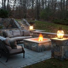 an outdoor fire pit surrounded by stone steps and seating area with lights on each side