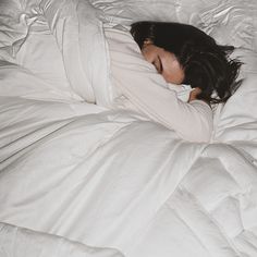 a woman is sleeping in a white comforter