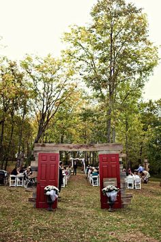 an outdoor ceremony set up with red doors and white chairs in front of it, surrounded by trees