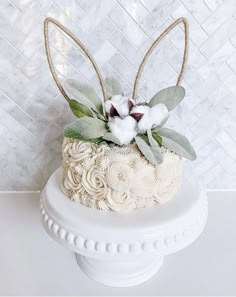 a white cake decorated with cotton flowers and leaves on top of a marble countertop