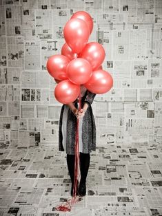 a woman holding red balloons while standing in front of a newspaper wall with black and white tiles