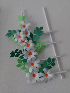 some paper flowers and sticks on a white wall with green leaves in the middle,