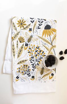 two white napkins with yellow and black flowers on them next to a bowl of dried berries