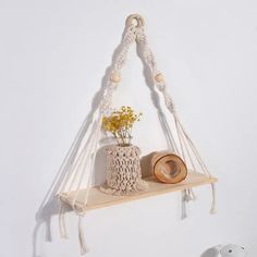 a wooden shelf with rope hanging from it and a vase filled with flowers on top