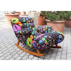 a colorful rocking chair sitting on top of a brick floor next to potted plants