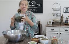 a woman standing in front of a counter holding a blender and mixing bowl filled with ingredients