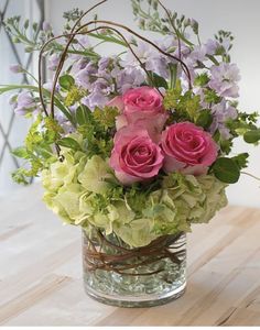 a glass vase filled with pink roses and greenery on top of a wooden table