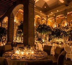 a dining room with tables and chairs covered in white linens, lit by candles