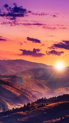 the sun is setting over mountains and hills