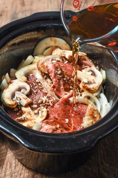 someone is pouring sauce on some food in a slow cooker with onions and mushrooms