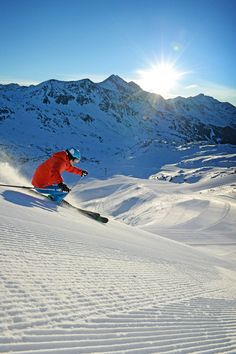 a man riding skis down the side of a snow covered slope with mountains in the background