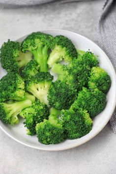 broccoli florets in a white bowl on top of a gray cloth