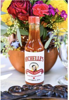 a bottle of hot sauce sitting on top of a table next to flowers and glasses