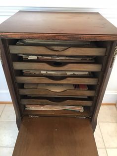 an old wooden cabinet with many drawers and papers on the bottom shelf, in front of a white wall