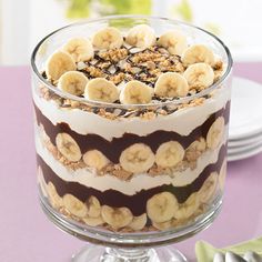 a layered dessert with bananas and chocolate sauce in a glass dish on a wooden table