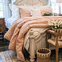 a bed with pink sheets and pillows in a bedroom next to two baskets filled with flowers