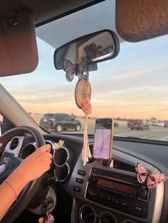 a woman driving a car with a cell phone hanging from the dash board and butterfly decorations on the dashboard