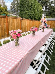 pink and white flowers are in vases on the long table with checkered cloth