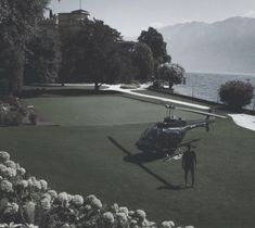 a man standing in front of a helicopter on top of a lush green field next to the ocean