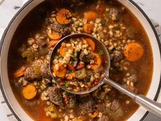 a ladle full of soup with meat, carrots and barley in the bowl