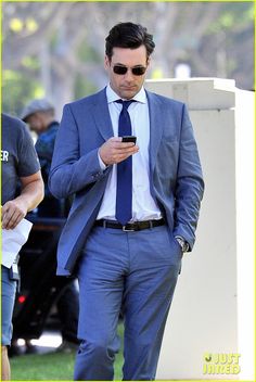 a man in a suit and tie is looking at his cell phone while standing outside