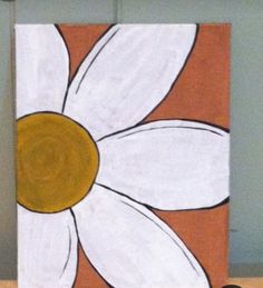 a painting of a white flower on an orange and brown background is sitting on a shelf