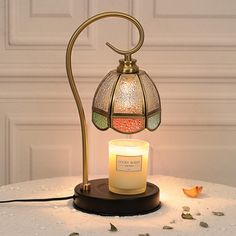 a lit candle sits on a table next to a decorative glass lamp that is shaped like a birdcage