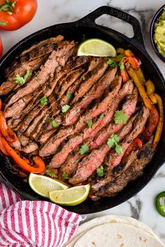 steak and vegetables in a cast iron skillet with limes, tomatoes, peppers, and cilantro