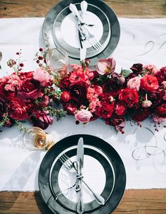 the table is set with silverware and red flowers on it, along with black plates