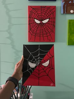 a person holding up some art work in front of a wall with spider - man paintings on it