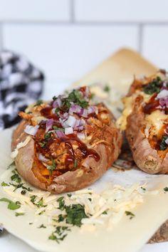 two baked potatoes sitting on top of a cutting board covered in cheese and toppings