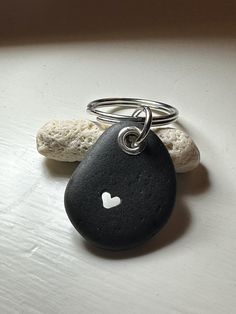 a black rock with a white heart on it is sitting next to a silver ring