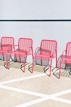 four red chairs sitting next to each other on a sidewalk near a white wall and cement floor