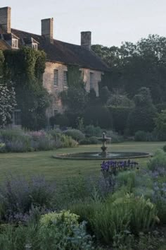 an old house is surrounded by greenery and lavenders in the foreground, with a fountain in the middle