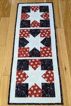 a quilted table runner with red, white and blue designs on it sitting on a wooden floor