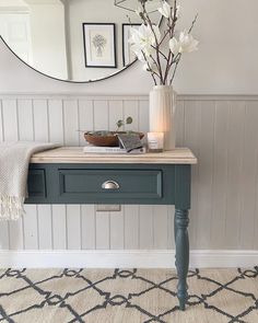 a table with flowers in a vase on top of it and a mirror above it