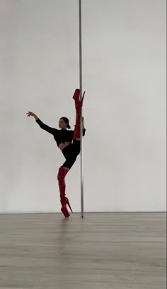 a woman in black shirt and red pants doing a trick with a pole on the floor