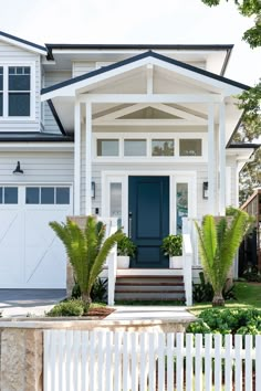 a white house with blue front door and steps leading up to the front door is surrounded by greenery