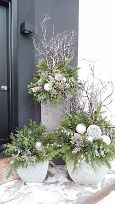 two white planters sitting on top of snow covered ground next to a black door